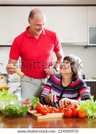 happy senior man in red and mature woman cooking lunch together in  kitchen