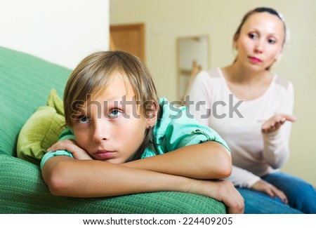 Ordinary mother scolding depressed teenager son in living room at home