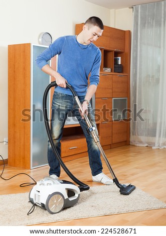 Smiling man  cleaning with vacuum cleaner on parquet floor in living room