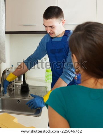 Woman  in green watching plumber\'s work with water lines