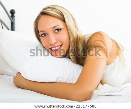Smiling long-haired woman in shirt lying on bed at bedroom