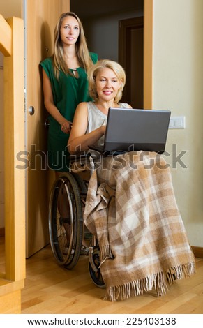 Happy woman in wheelchair with female assistant working on laptop indoor