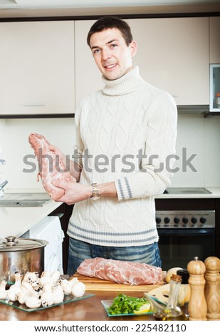 Smiling guy with raw meat at domestic kitchen