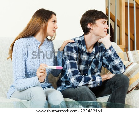Sad worried woman with pregnancy test with unhappy man at home interior