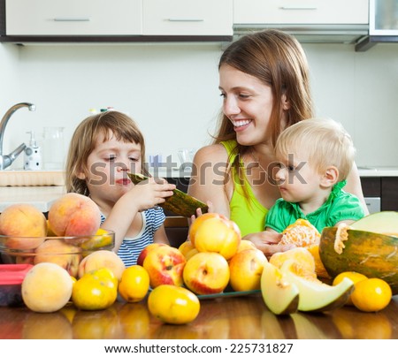 Ordinary mother with children eating melon and peaches over table at home interior