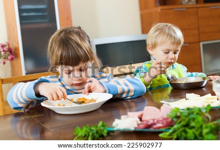 serious  children eating food at wooden table in home interior