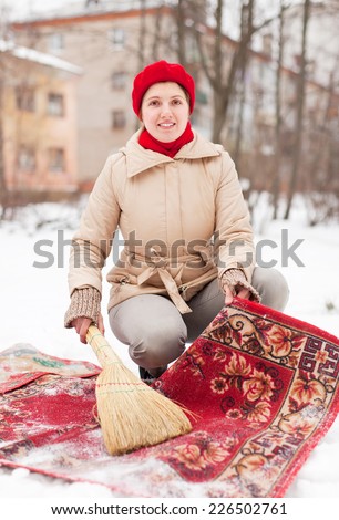 woman in red cap cleans carpet with snow in winter