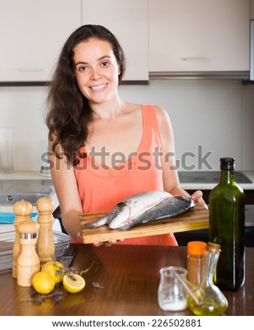 Young smiling woman cooking fish in home kitchen