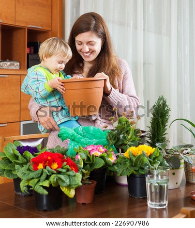 Smiling young mother and child with flowering plants in pots at home