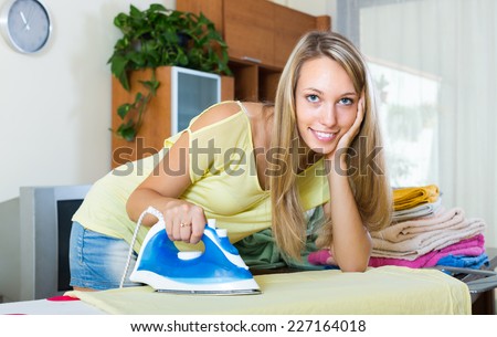 Young blonde girl ironing with iron and ironing board at home