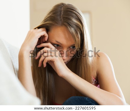 Sad and lonely woman with long hair sitting on couch at home