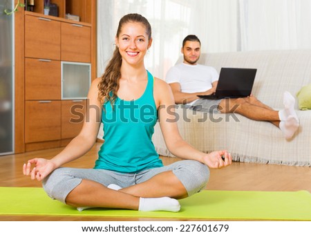Smiling young female in yoga position and lazy guy on sofa