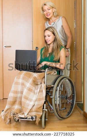 Smiling mature woman and handicapped girl using laptop indoor. Focus on young