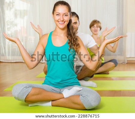 Happy young people doing yoga on mats in gym