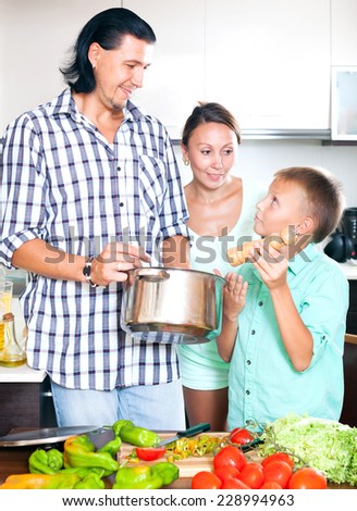 Happy man and woman with boy adding spices or salt to the pot and in home kitchen