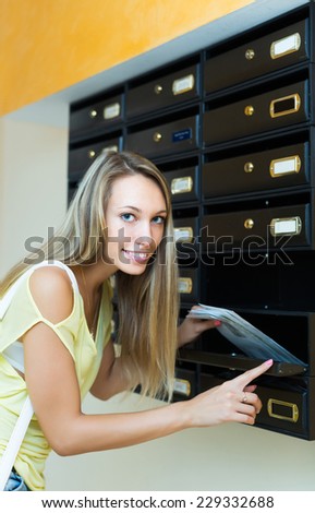Blonde smiling housewife checking up letter-box indoor