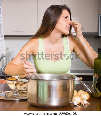 Young unpleased housewife pinched her nose avoiding bad smell from pan
