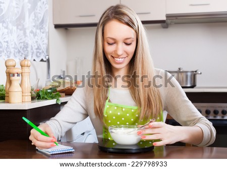 Happy woman weighing cottage cheese on kitchen scales