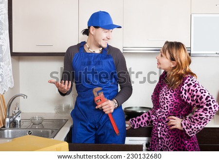 happy repairman in uniform  repairing a running water for woman in kitchen