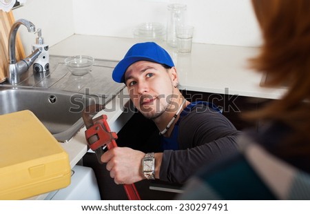 Plumber repairing a kitchen sink for housewife