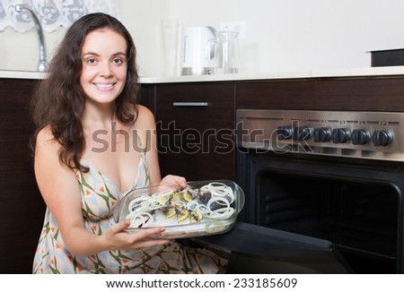 Smiling woman putting  fish in oven at home kitchen