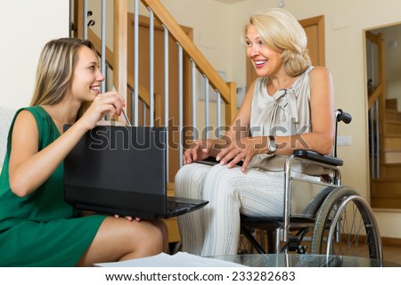 Female social worker with laptop questioning smiling handicapped aged woman. Focus on mature