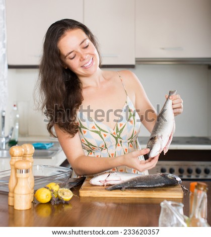 Young smiling brunette woman with fish at home kitchen