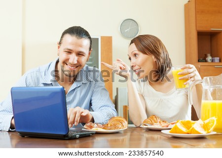 Happy couple looking e-mail in laptop during breakfast time at home