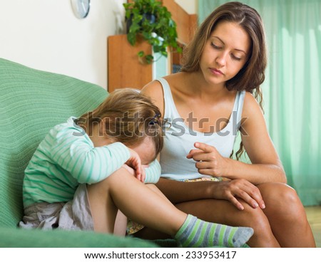 Unpleased young mother scolding crying little daughter at home