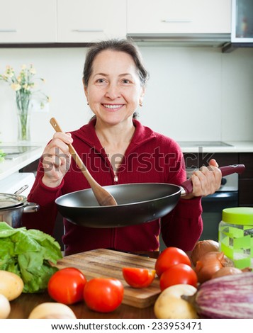 Smiling mature woman cooking  with skillet in domestic kitchen