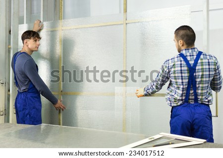 Two careful young workmen cutting glass for windows at workshop