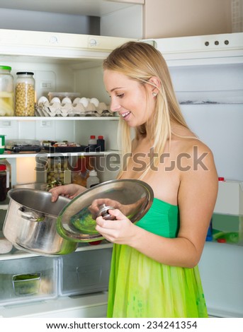 Happy hungry girl with pan near fridge  at home
