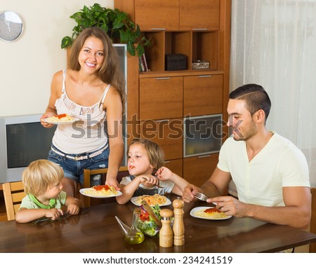 Happy young family of four having lunch with spaghetti at home. Focus on man