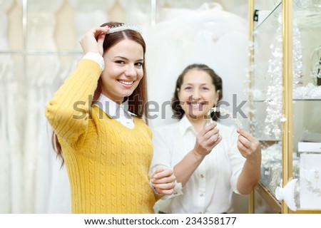 Shop assistant  helps the bride in choosing bridal diadem at shop of wedding fashion. Focus on girl