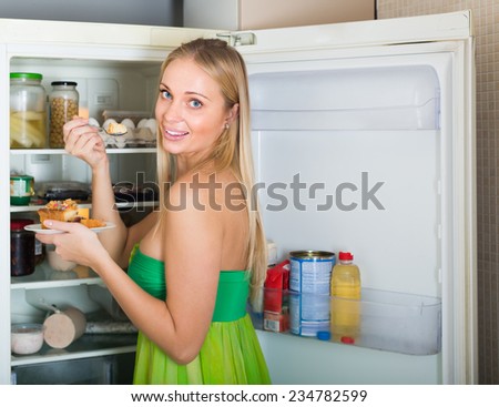 Young blonde woman eating cake from fridge at home