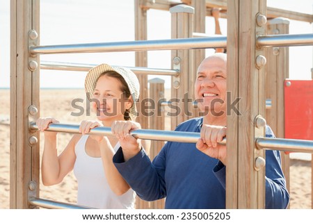 Mature couple training on pull-up bar in summer
