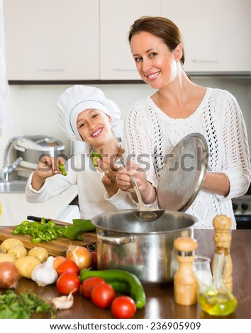 Portrait of daughter and smiling mom with vegetables and casserole at domestic kitchen. Focus on woman