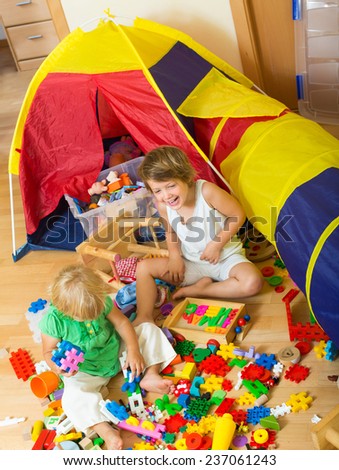 Two smiling cute little sisters playing with toys together in home interior