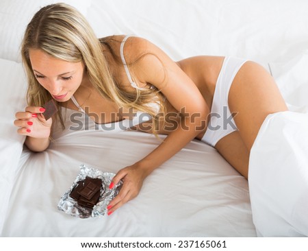 Long-haired female eating  chocolate  in bed at home