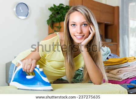 Smiling blonde girl ironing with iron and ironing board at home