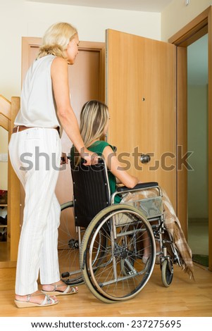 Elderly mother helping handicapped girl to enter the apartment