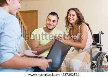 Female social worker consulting smiling young woman in invalid chair and husband. Focus on man