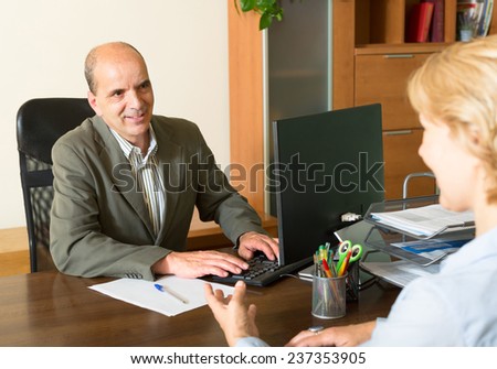 Two positive older people are discussing something at the computer in the office