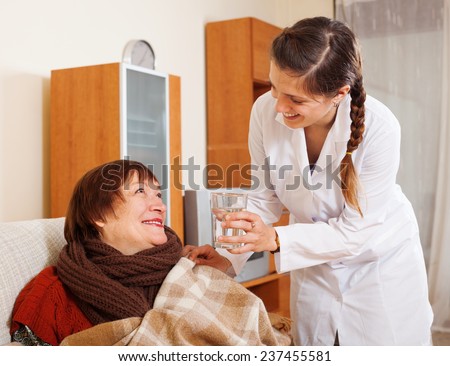 Smiling nurse in uniform caring for happy mature woman in living room at home