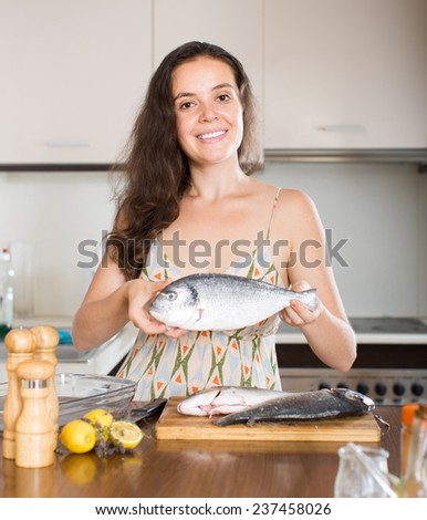 Young smiling housewife cooking fish in home kitchen