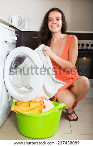 Smiling girl cheking white clothes near washing machine  at home