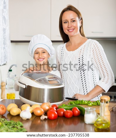 Portrait of smiling girl and her mom with rice cooker at home kitchen