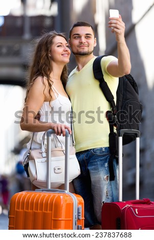 Young man and woman with luggage doing selfie during city tour at vacation