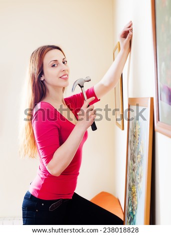 Smiling  woman hanging  art picture on wall