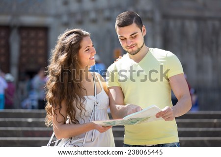 Man and woman in shorts walking through street with city map in hands